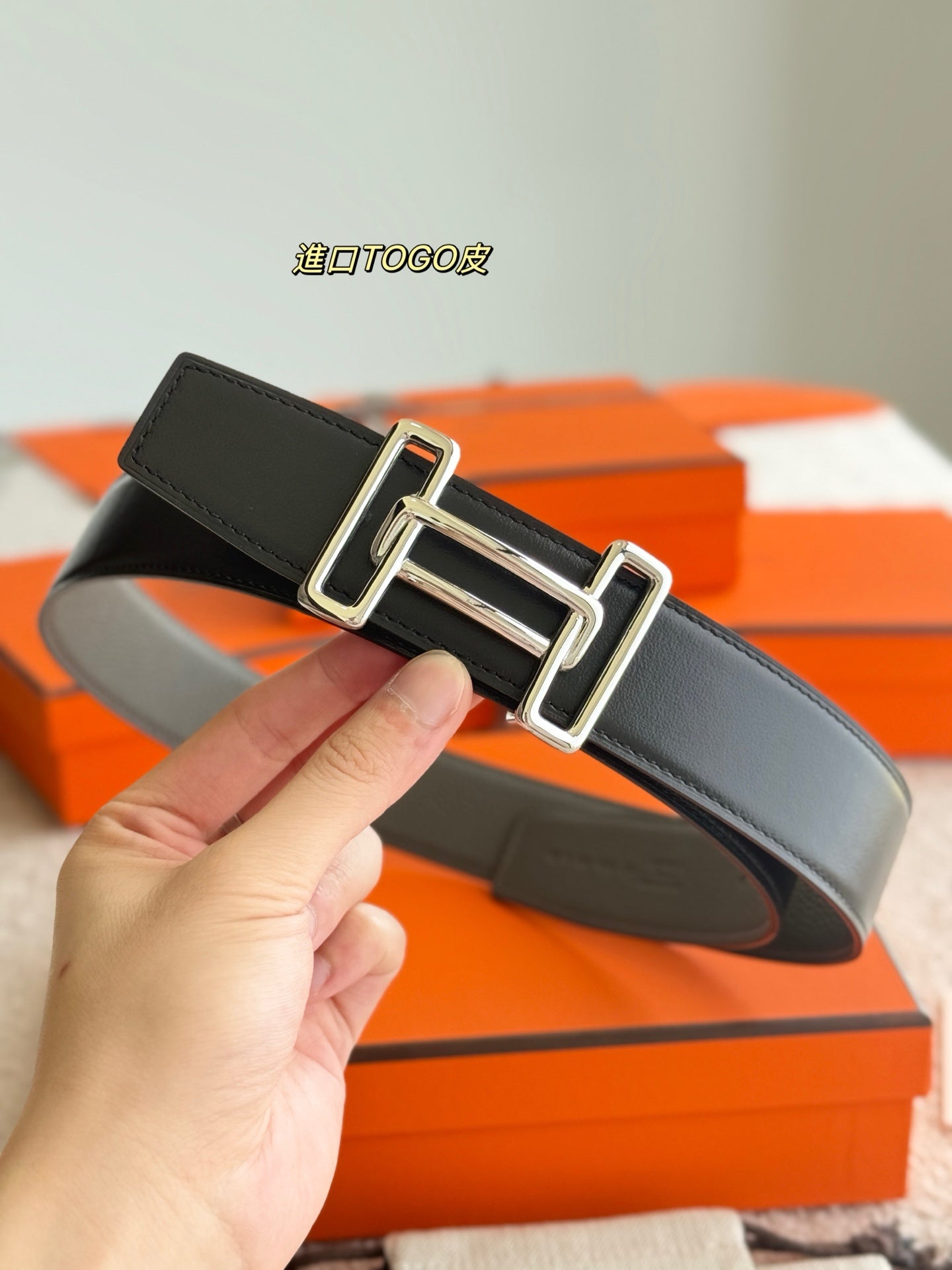 Hermes reversible leather belt, dark strap with silver buckle, held in hand