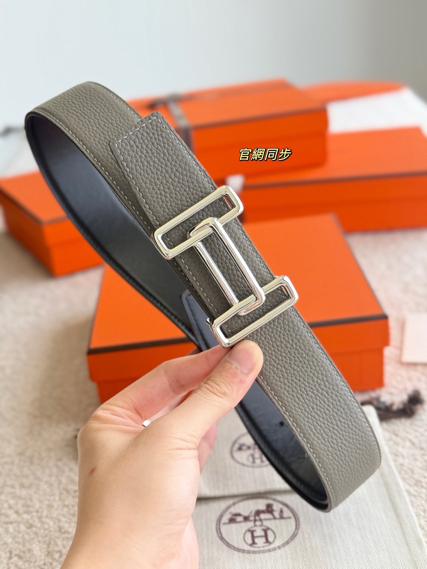 Hermes reversible leather belt, light gray strap with silver buckle, held in hand