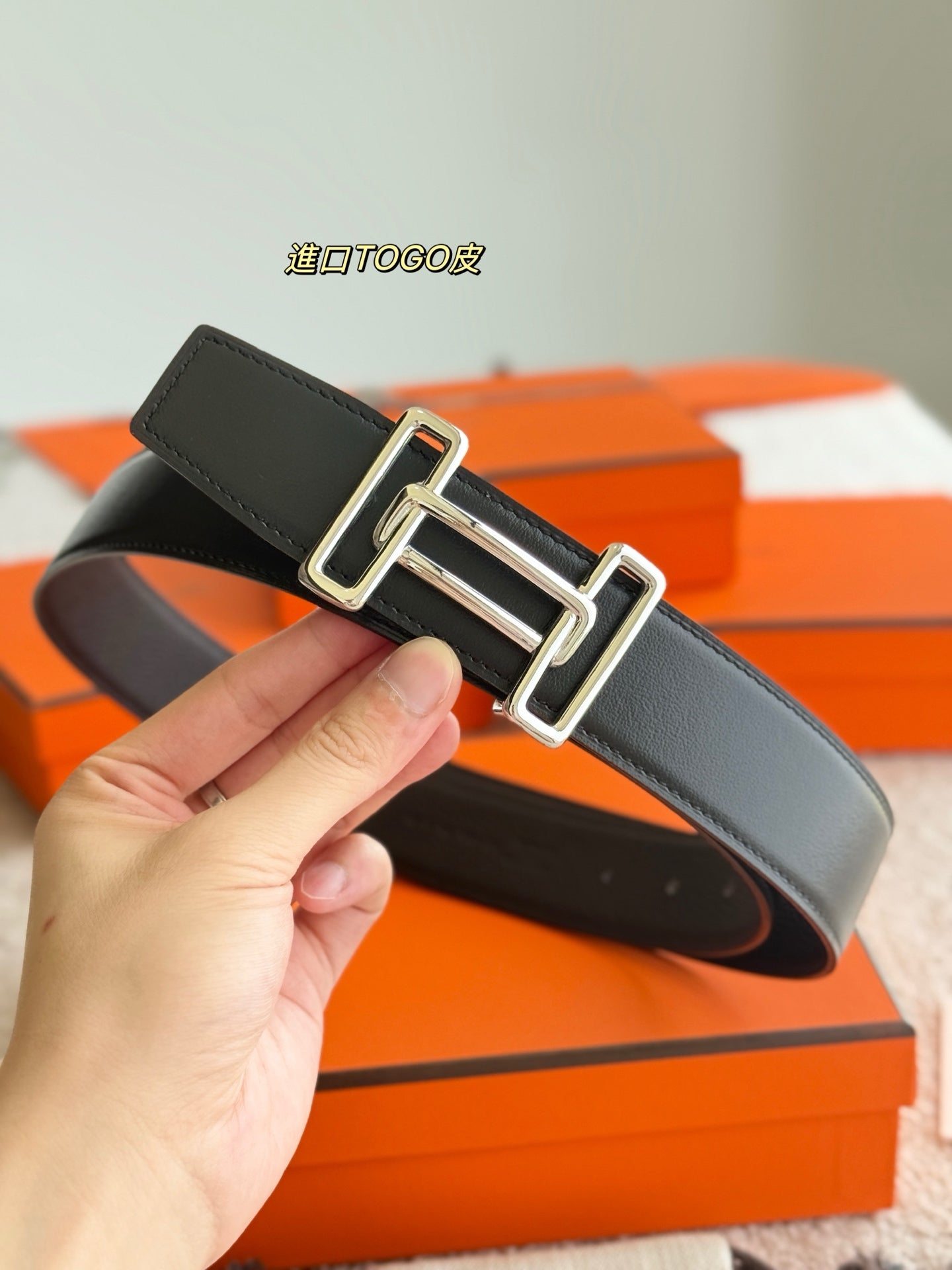 Hermes dark leather belt with silver buckle, hand holding close-up