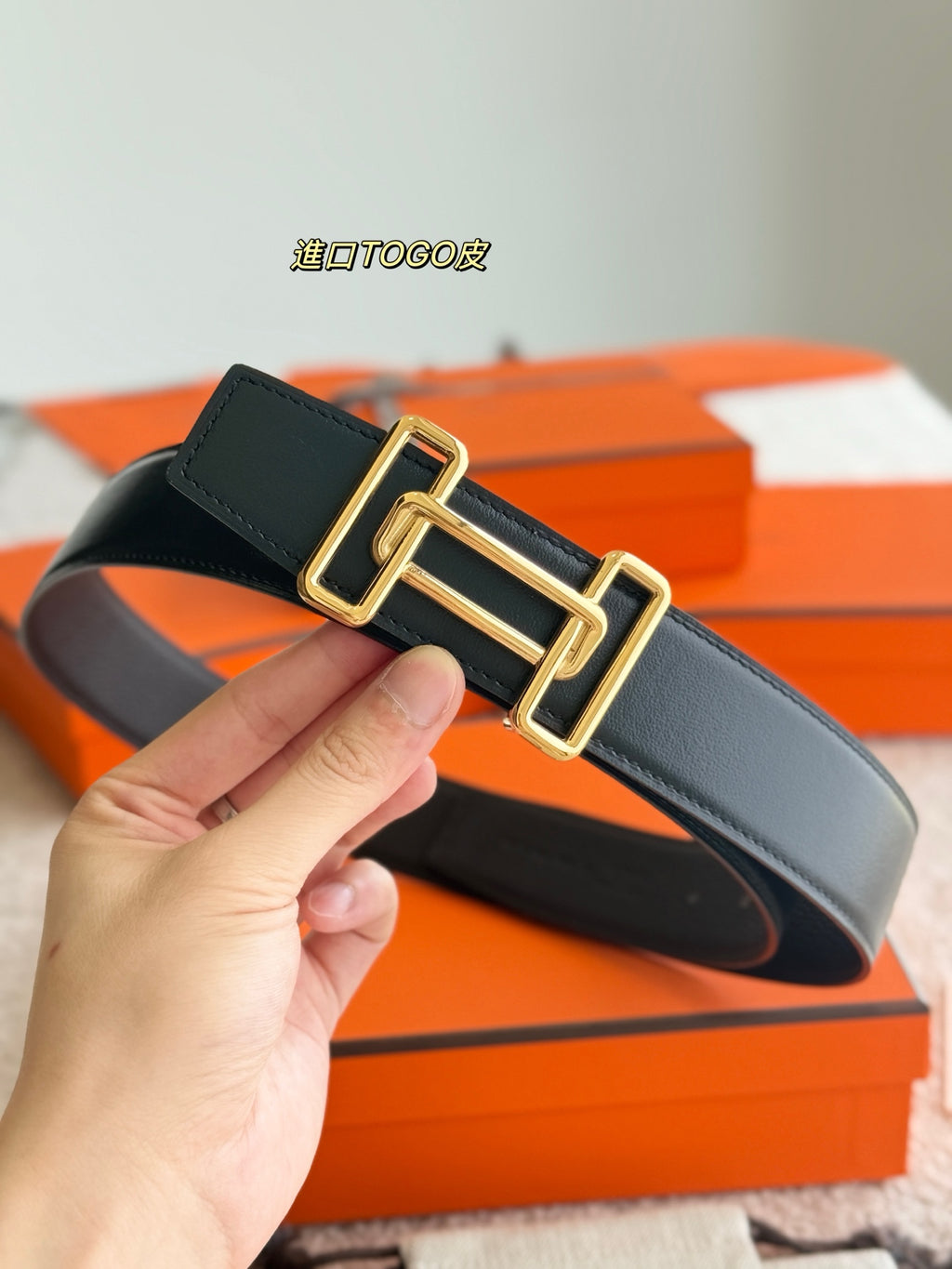Dark leather belt held diagonally, gold double-buckle hardware on strap.
