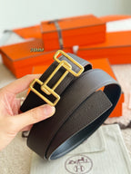 Hand holding dark leather belt, close-up on gold buckle and textured strap.