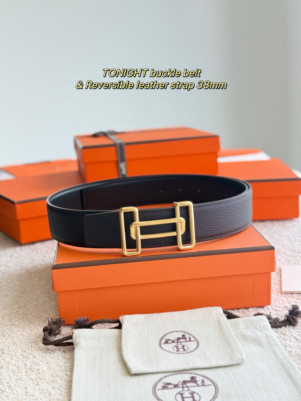 Dark leather belt with gold rectangular buckle, reversible strap detail, flat lay.