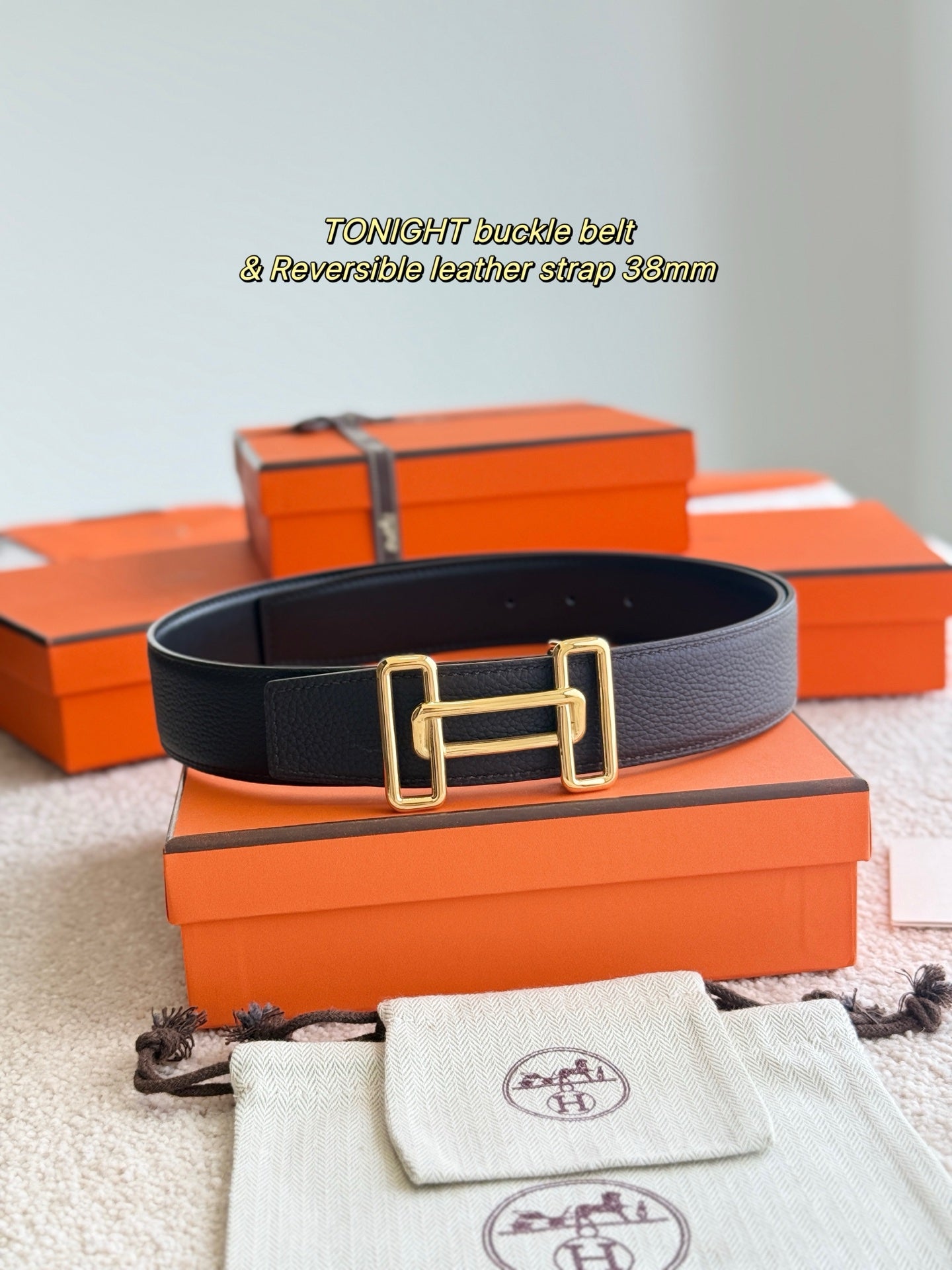 Dark leather belt with gold rectangular buckle, reversible strap detail, flat lay.