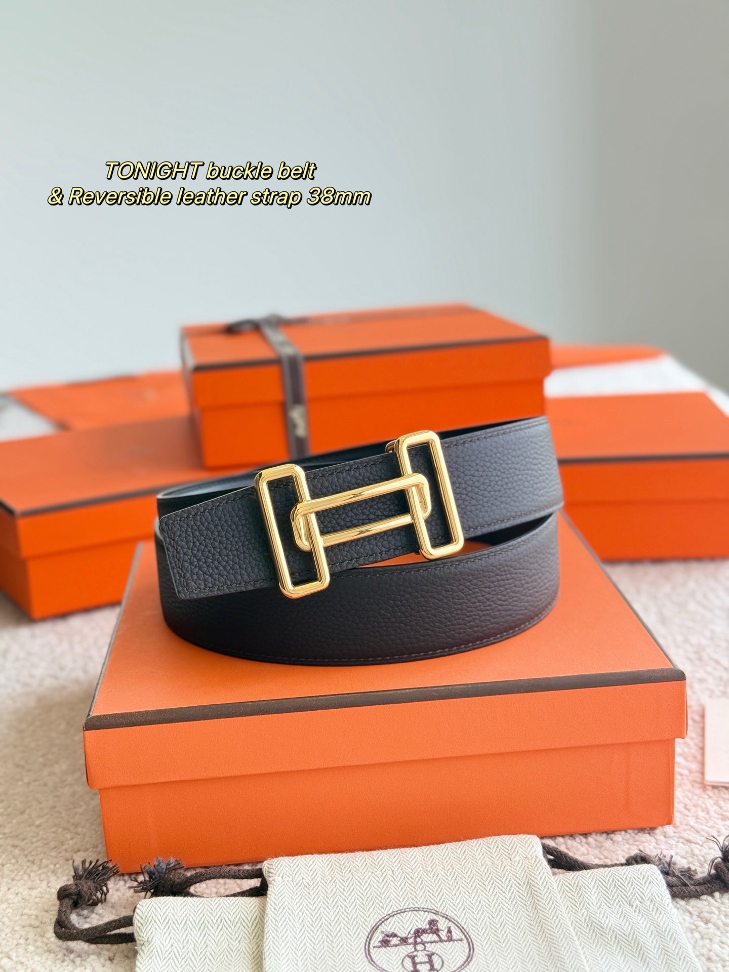 Black leather belt with gold buckle centered, shown on box and drawstring pouch.