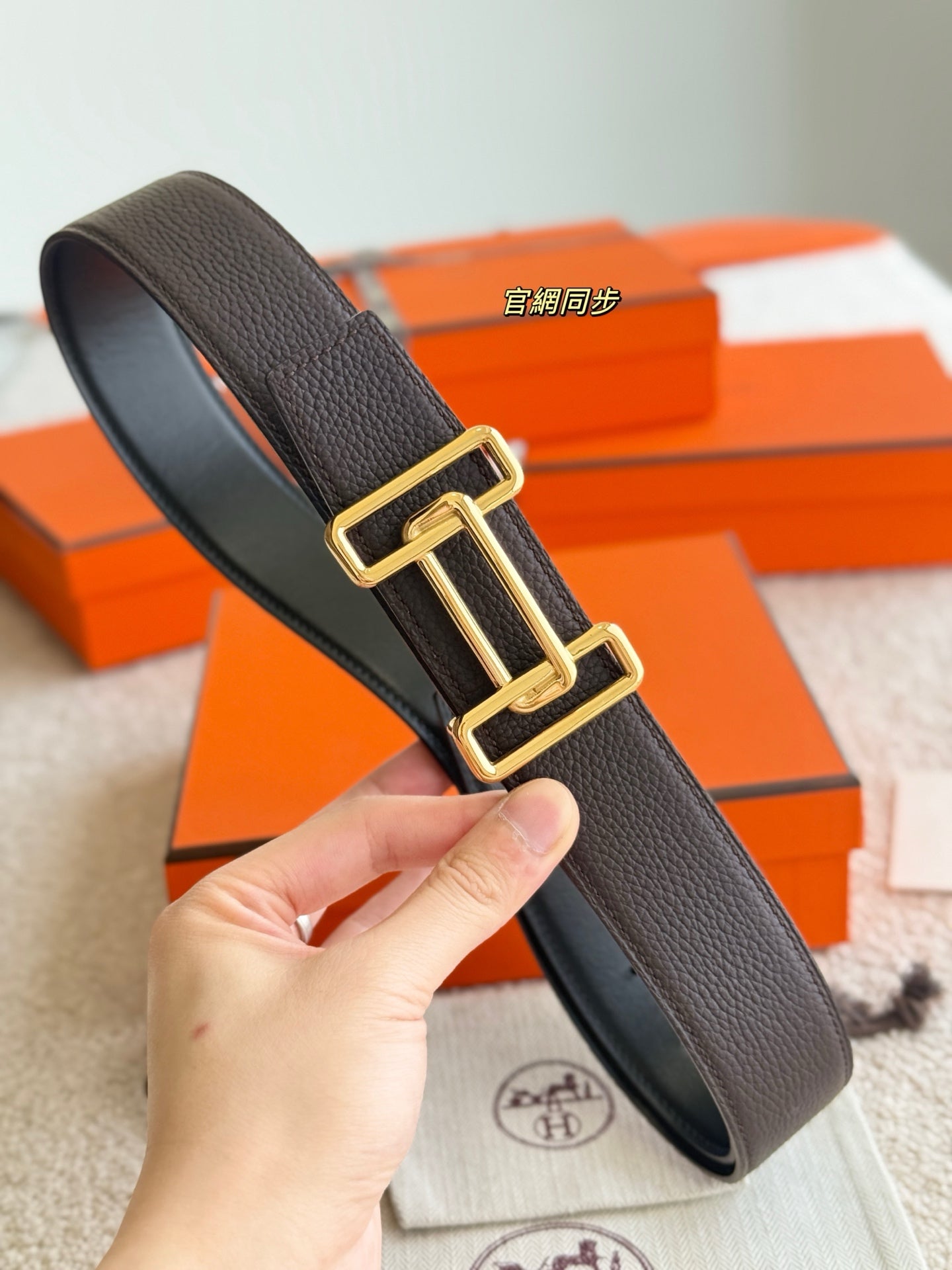 Dark leather belt held upright with gold buckle, smooth grain strap.