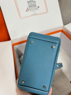 Blue textured leather mini handbag with snap buttons on back; strap peeks beside.