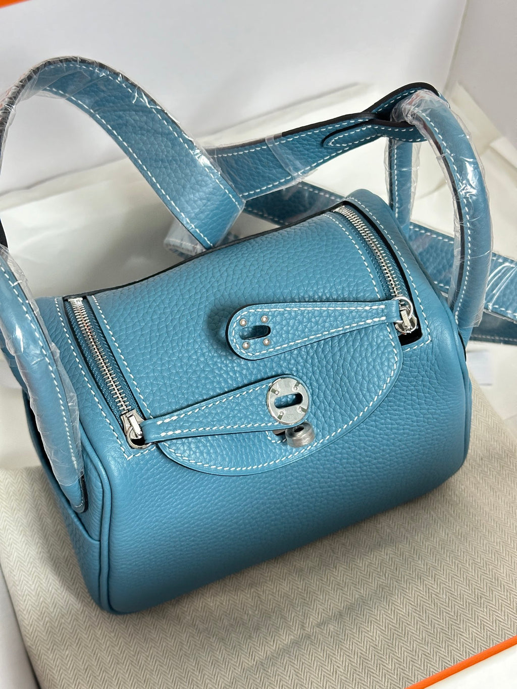 Blue leather mini handbag with front strap detail and double buckle closure; in box.