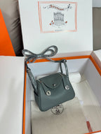 Hermes bag, dark teal pebbled leather, flap with round studs, displayed in gift box.