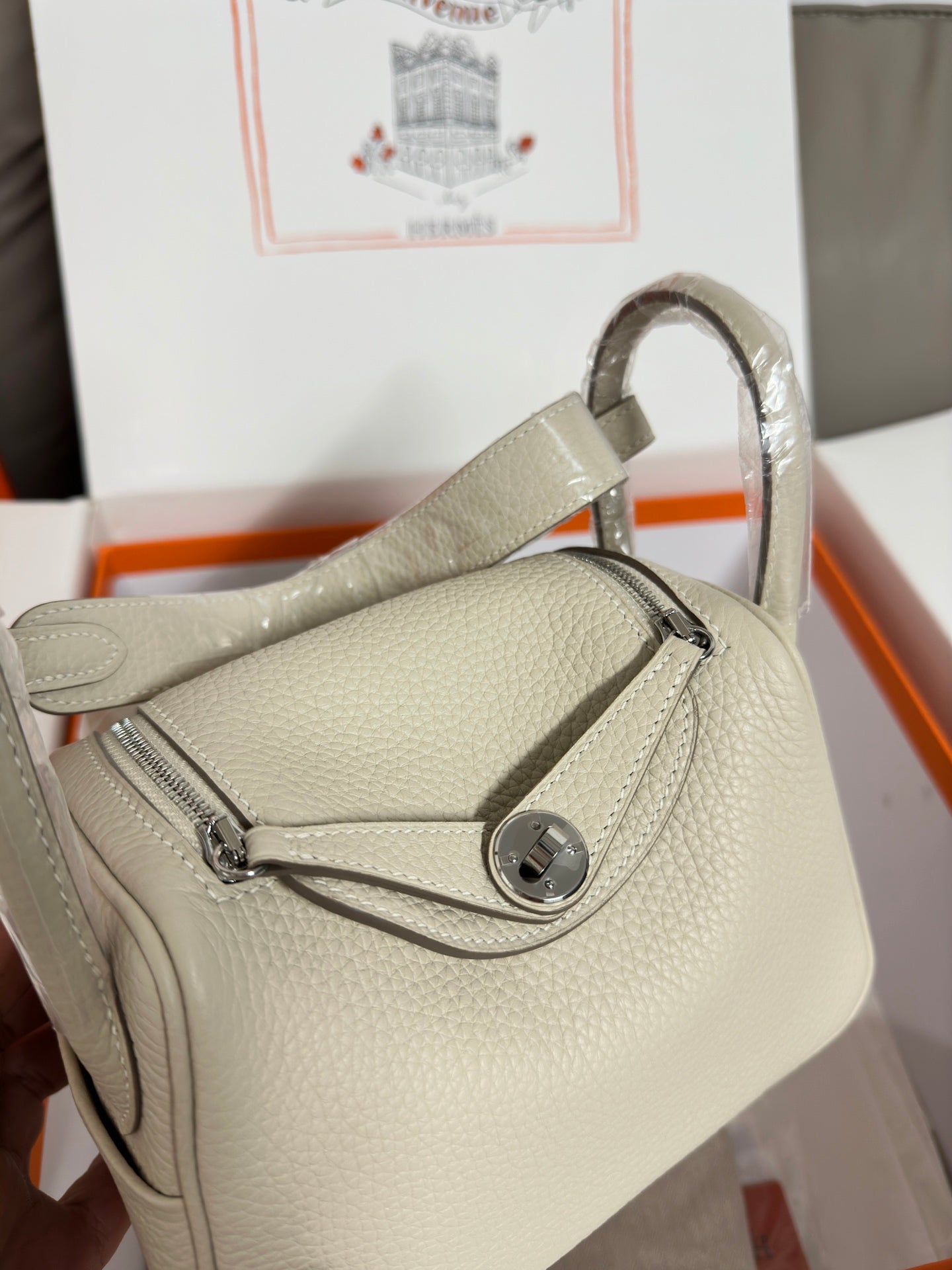 Hermes bag close-up: light beige textured leather, oval front clasp, and handle
