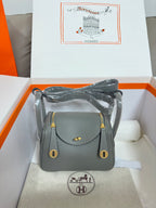 Gray leather handbag with gold-tone flap, top handle, and adjustable shoulder strap.