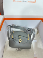 Gray leather crossbody handbag with gold-tone flap and shoulder strap, boxed.