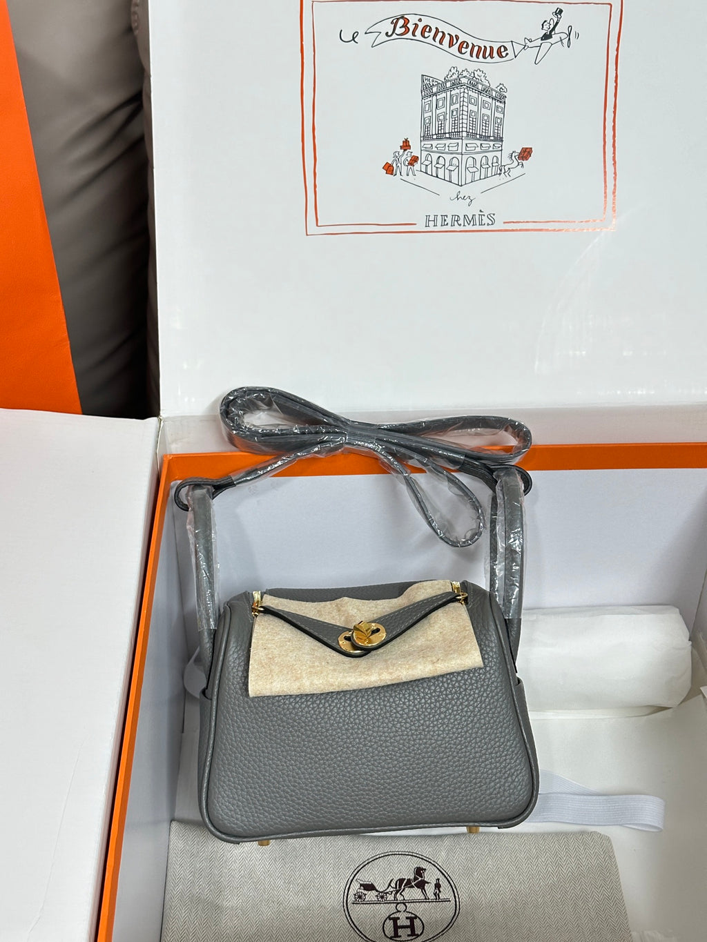 Gray leather handbag with tan canvas front flap and gold-tone clasp, angled view.