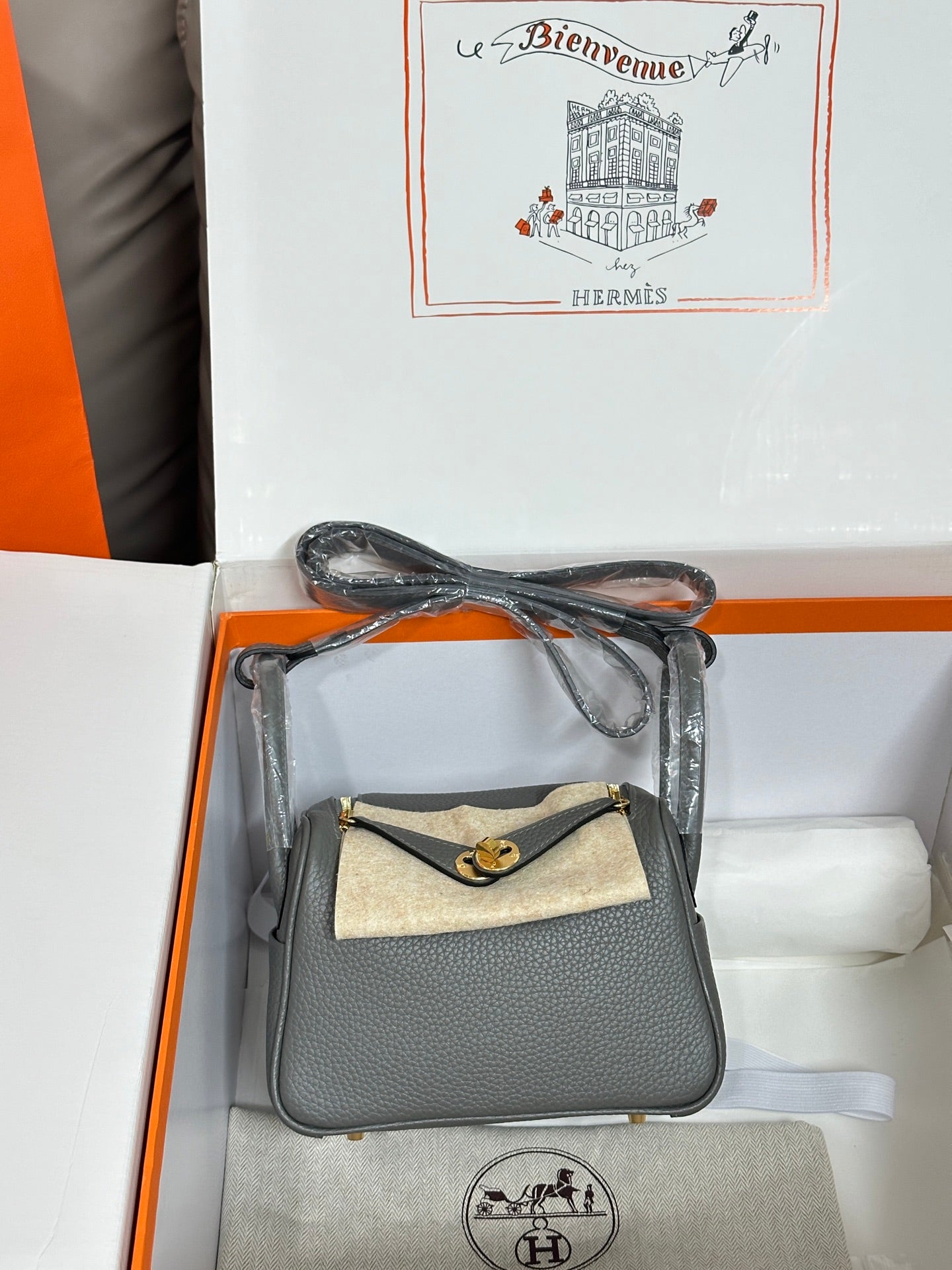 Gray leather handbag with tan canvas front flap and gold-tone clasp, angled view.