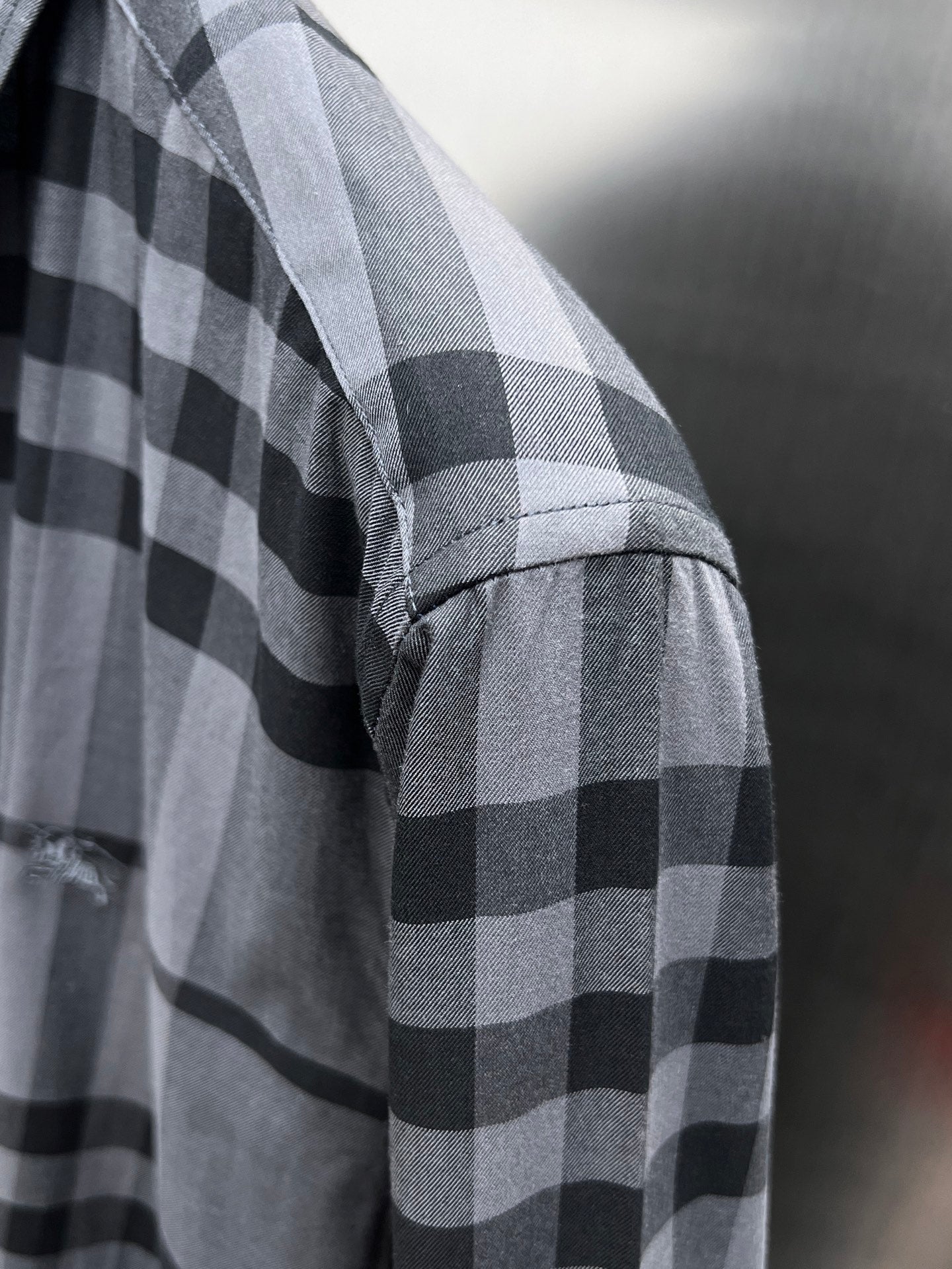 Plaid button-up shirt sleeve in gray and black check pattern, side view