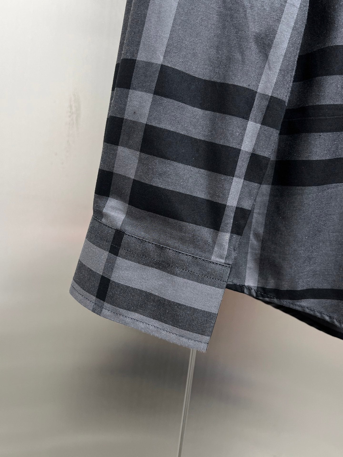 Plaid button-up shirt hem with gray and black check pattern, side view