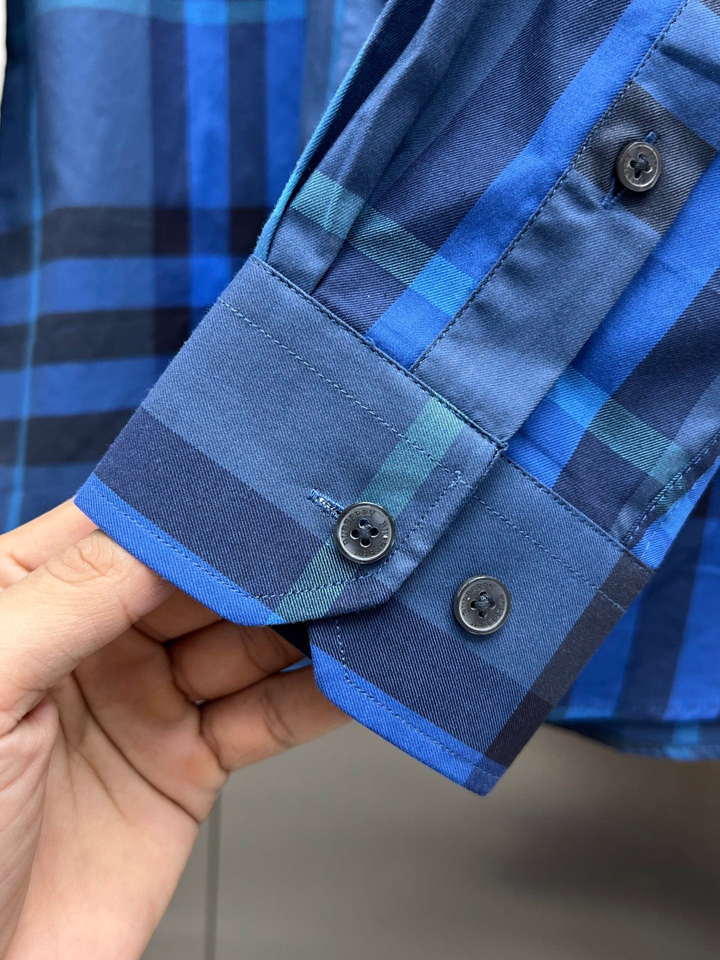 Blue/black plaid long-sleeve shirt cuff with two dark buttons.