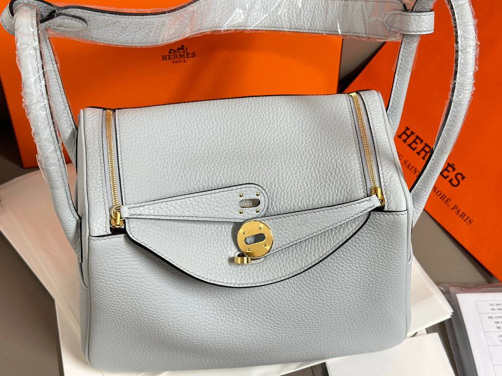 Light blue leather handbag with front flap, gold lock, and adjustable shoulder strap.