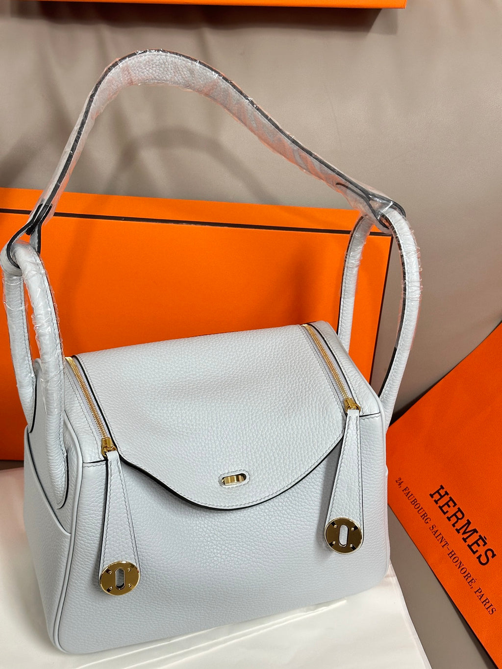 Light blue leather handbag with top handles, front flap, and gold hardware details.