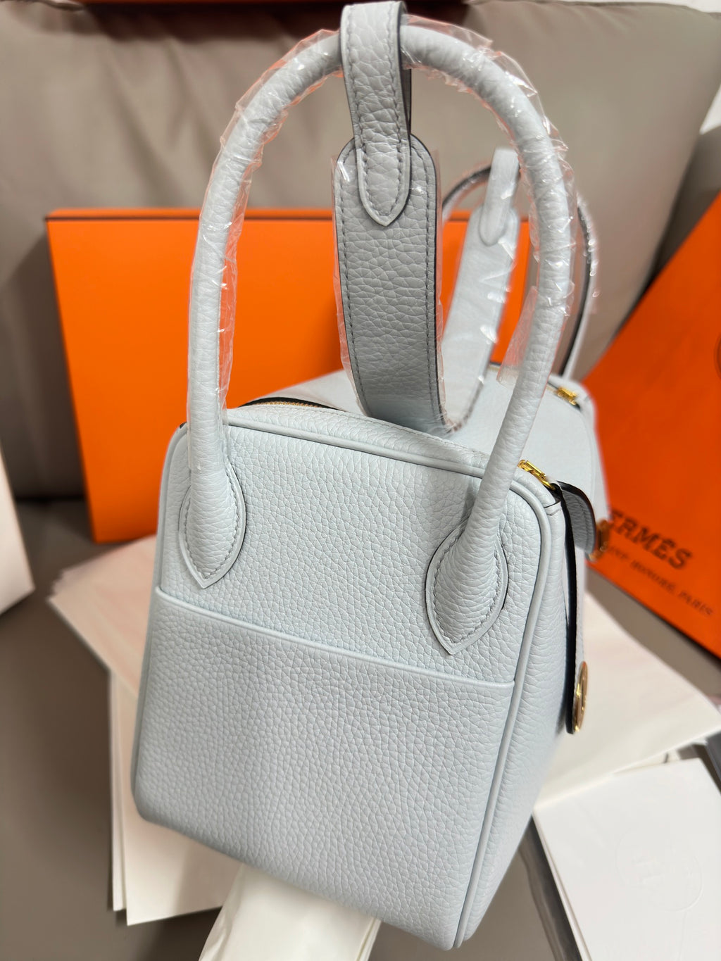 Light blue leather satchel with tall top handle, flap front, and gold accents.
