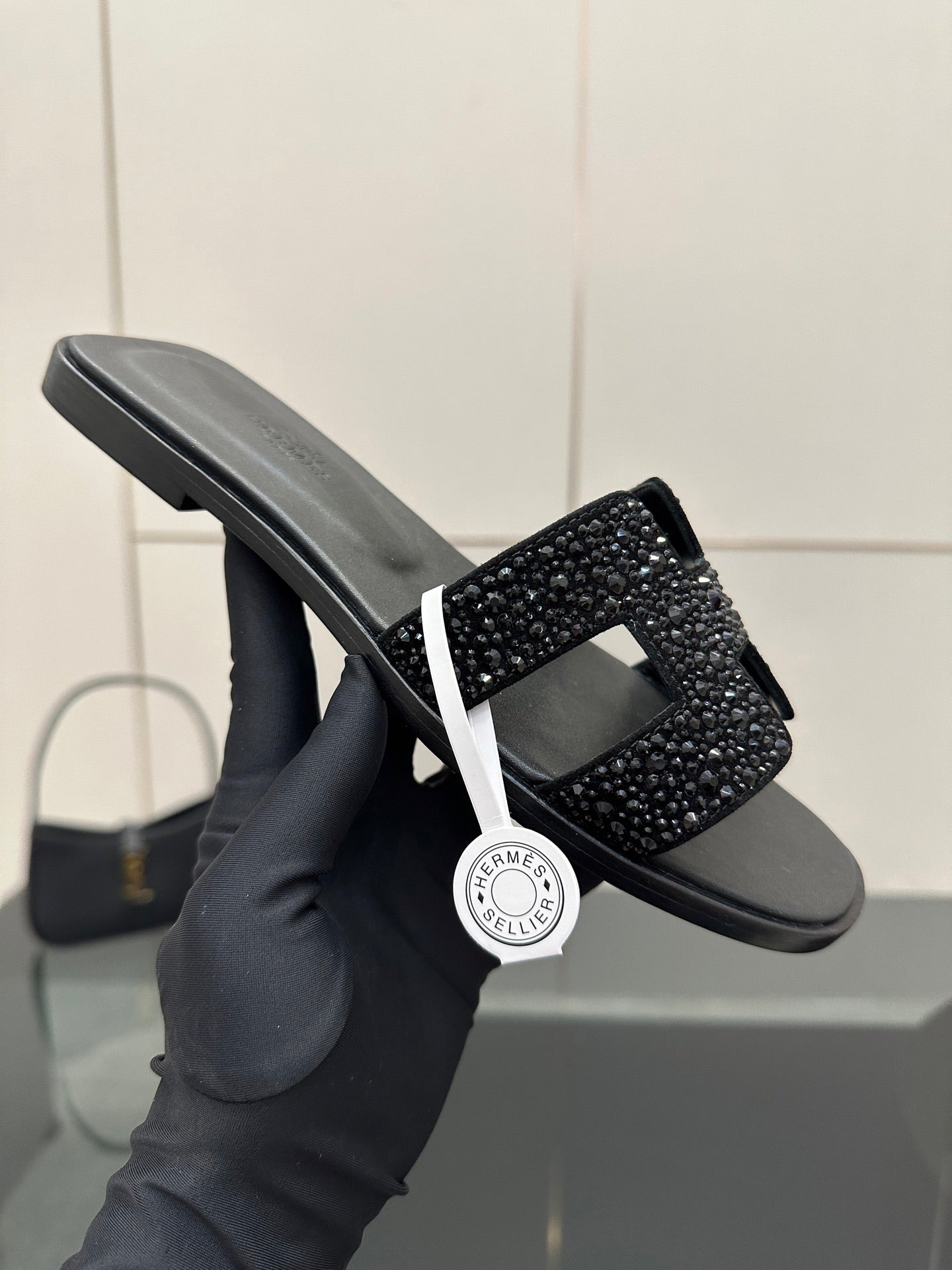 Black slide sandal held in gloved hand, rhinestone strap across top