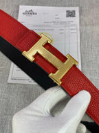 Hermes belt close-up: gold H buckle on red strap with black backing.