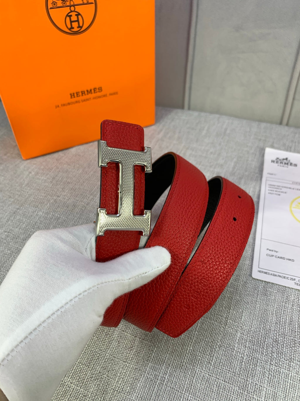 Hermes belt close-up: red leather with gold buckle hardware and strap holes.