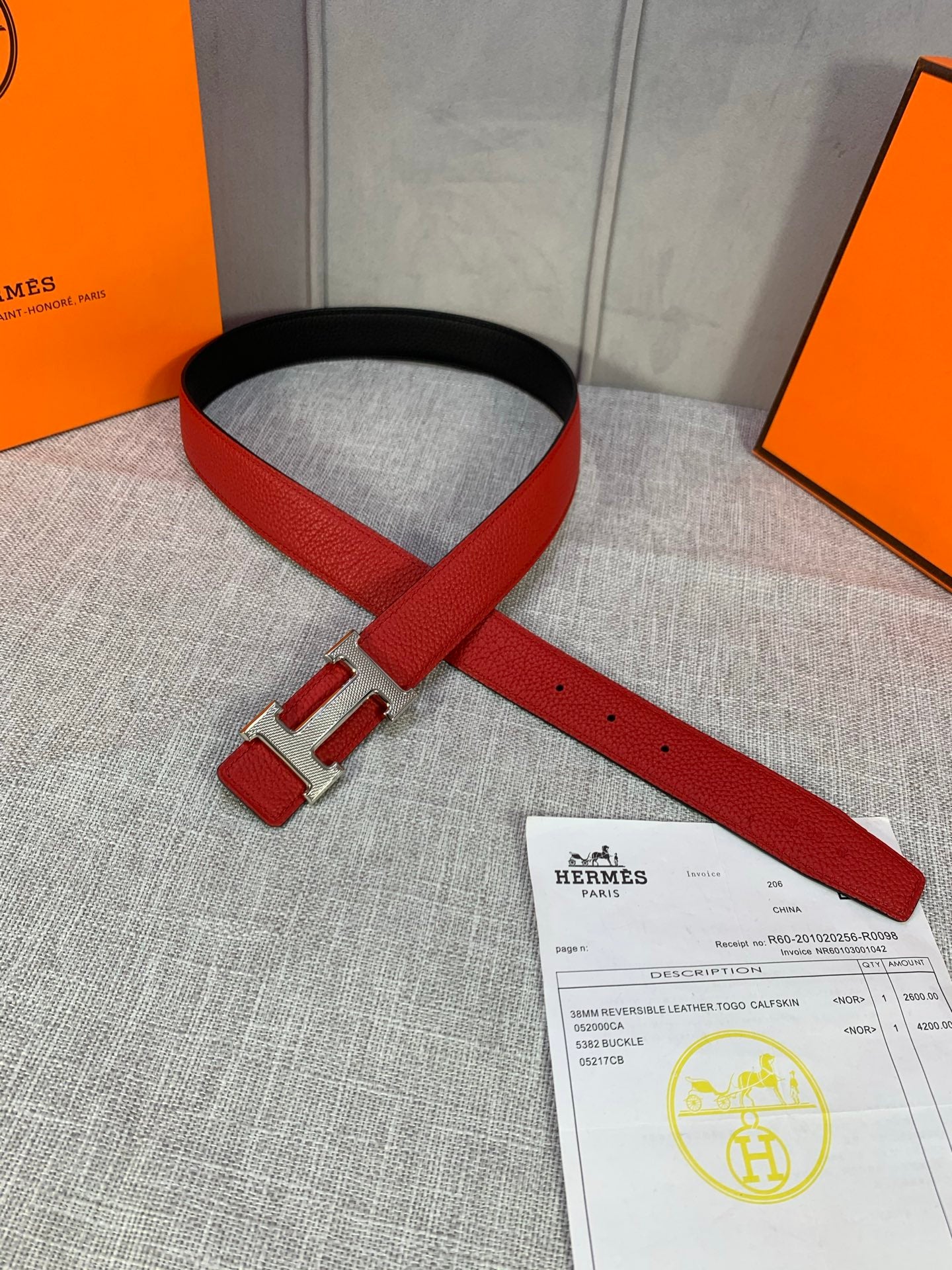 Hermes belt flat with red strap, gold buckle hardware, black edge and hole details.