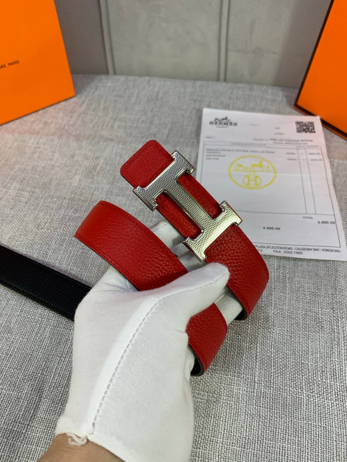 Hermes belt showing red leather strap with silver-toned buckle and black backing.