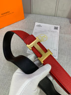 Hermes belt angled view with red leather, gold H buckle, and black reverse side.