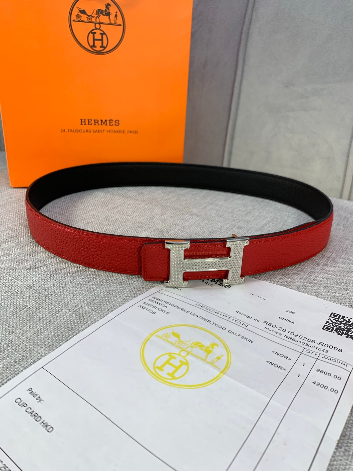 Hermes belt with red leather strap and silver-toned H buckle over black inner lining.