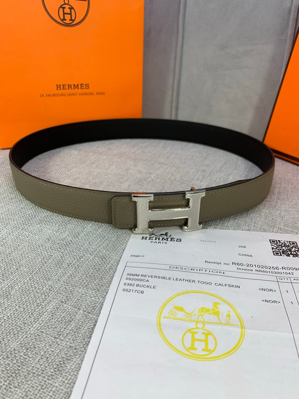 Olive leather belt with silver H buckle, resting on documents