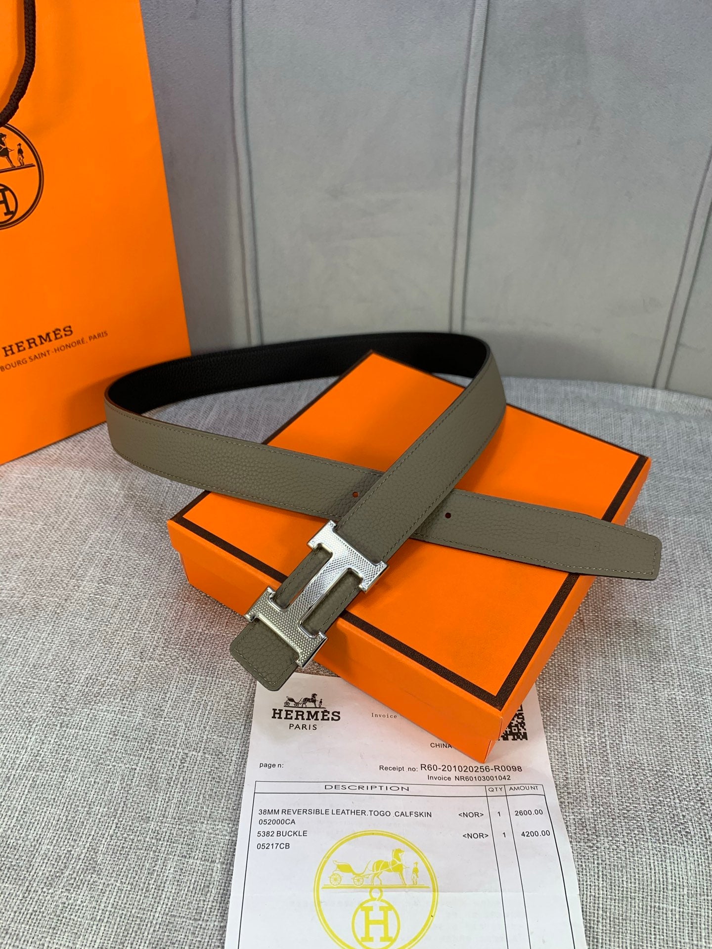 Reversible leather belt with olive strap and silver H buckle, on paperwork