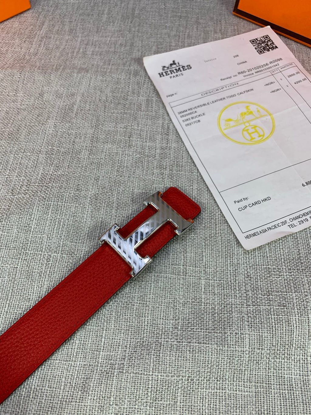 Red leather belt with silver buckle and red strap end, beside folded certificate paper.