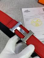 Red and black reversible belt with silver H buckle detail, close-up view in hand.