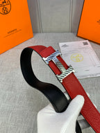 Red and black reversible belt with silver H buckle, held over the gray fabric.
