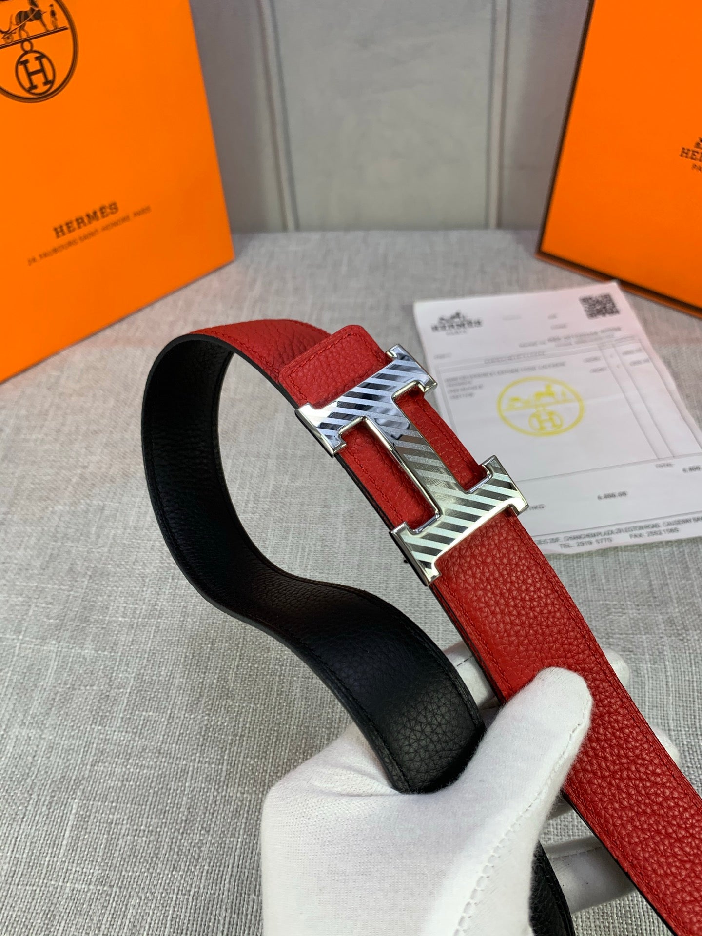 Red and black reversible belt with silver H buckle, held over the gray fabric.