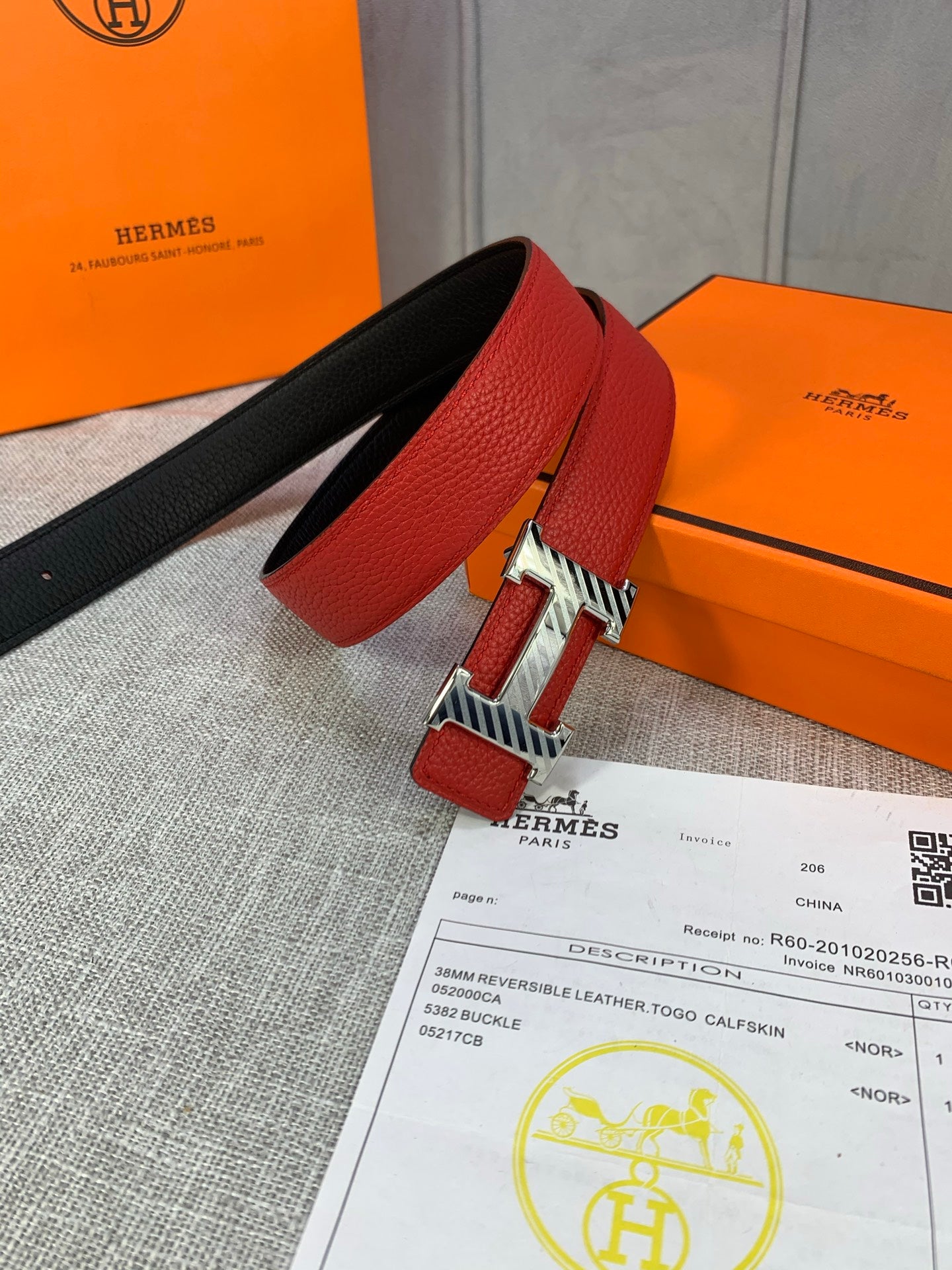 Red and black reversible leather belt with silver buckle, laying across paperwork.