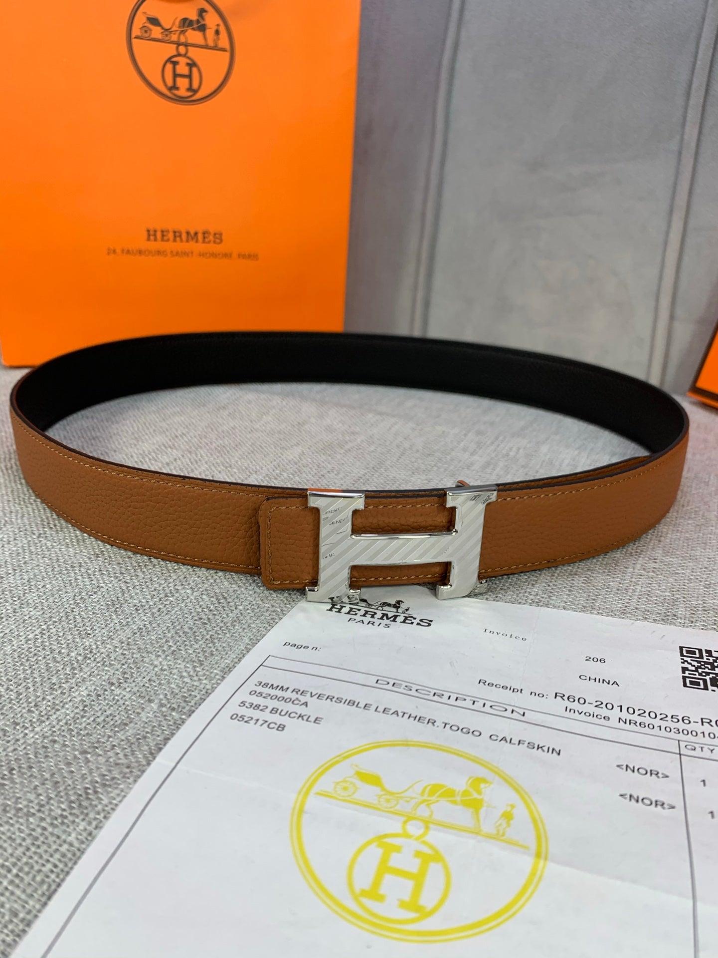 Brown leather belt with silver H buckle and keeper, flat on paperwork