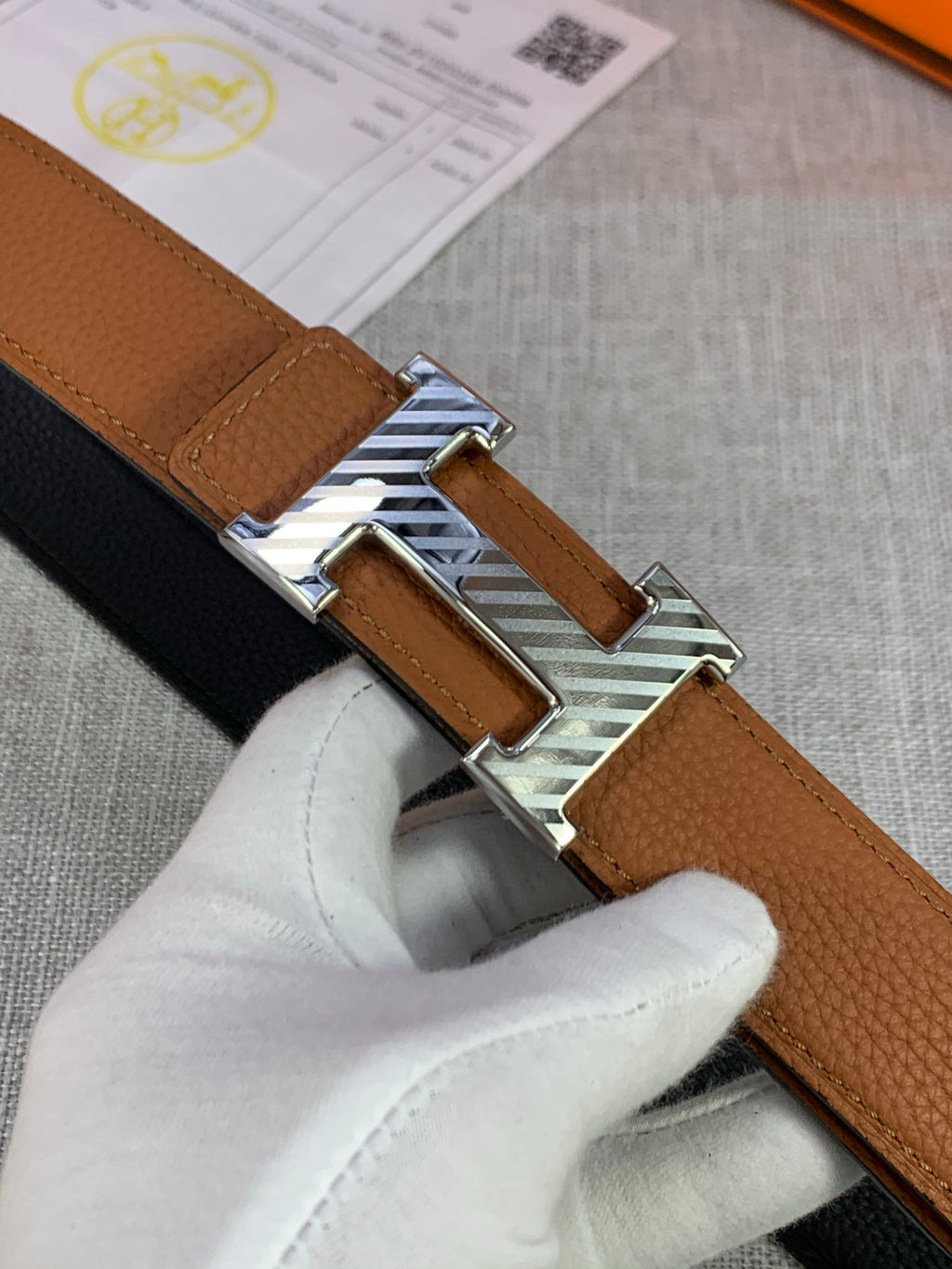 Brown leather belt with silver buckle and stitched keeper, close-up