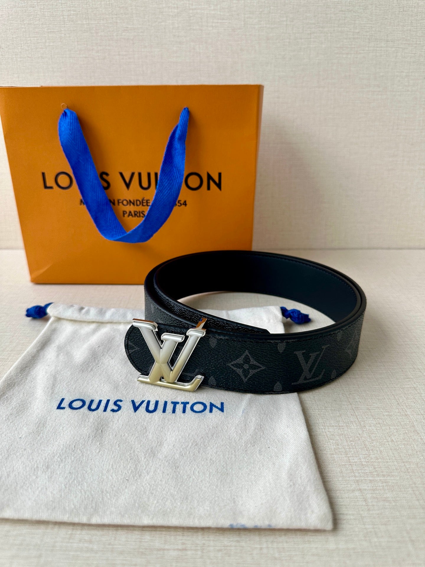Louis Vuitton belt on dust bag: dark monogram strap and silver buckle, angled