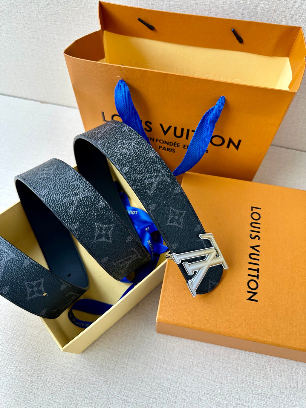 Louis Vuitton belt laid in open box: dark monogram straps with silver buckles
