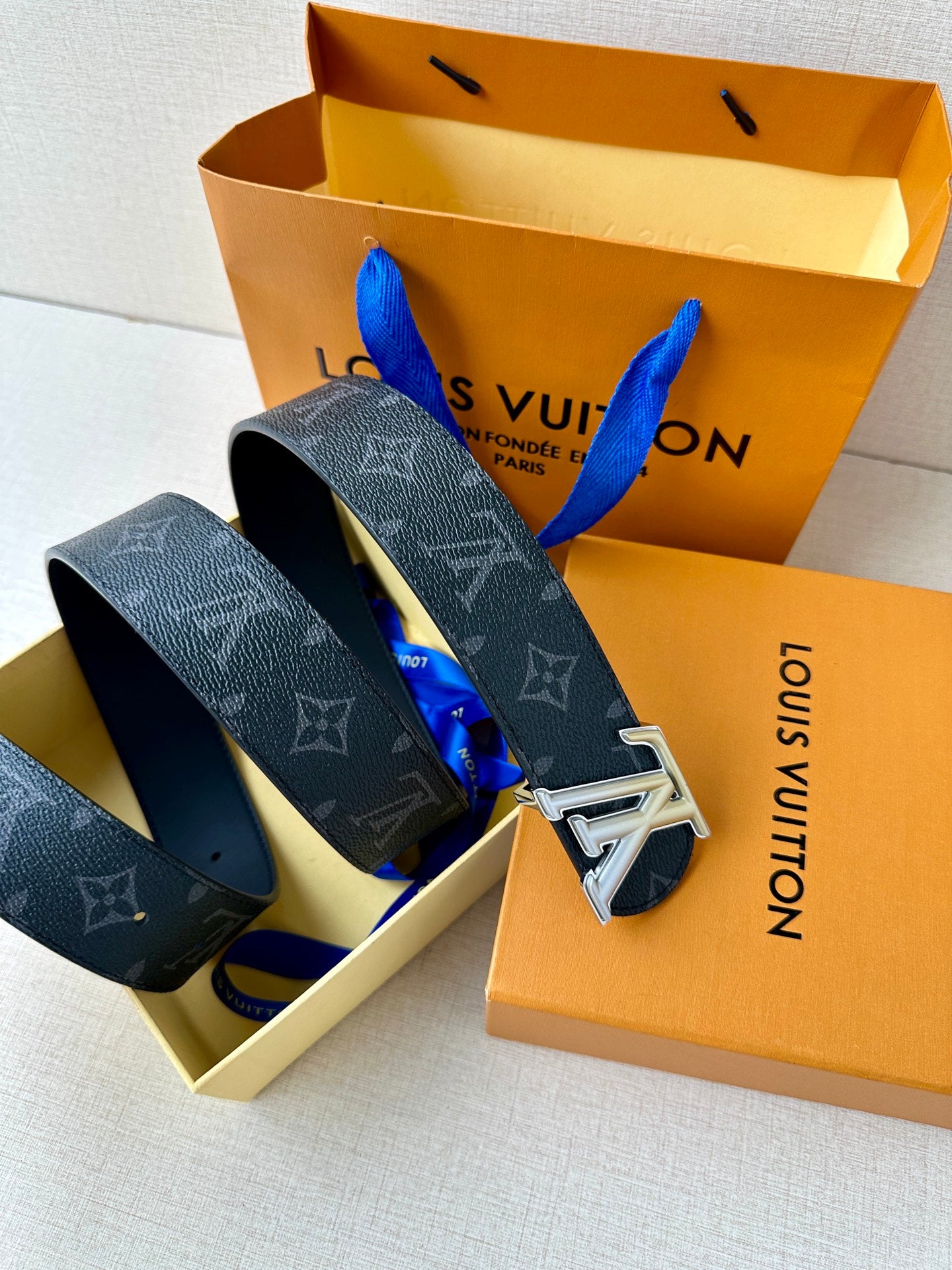 Louis Vuitton belt laid in open box: dark monogram straps with silver buckles