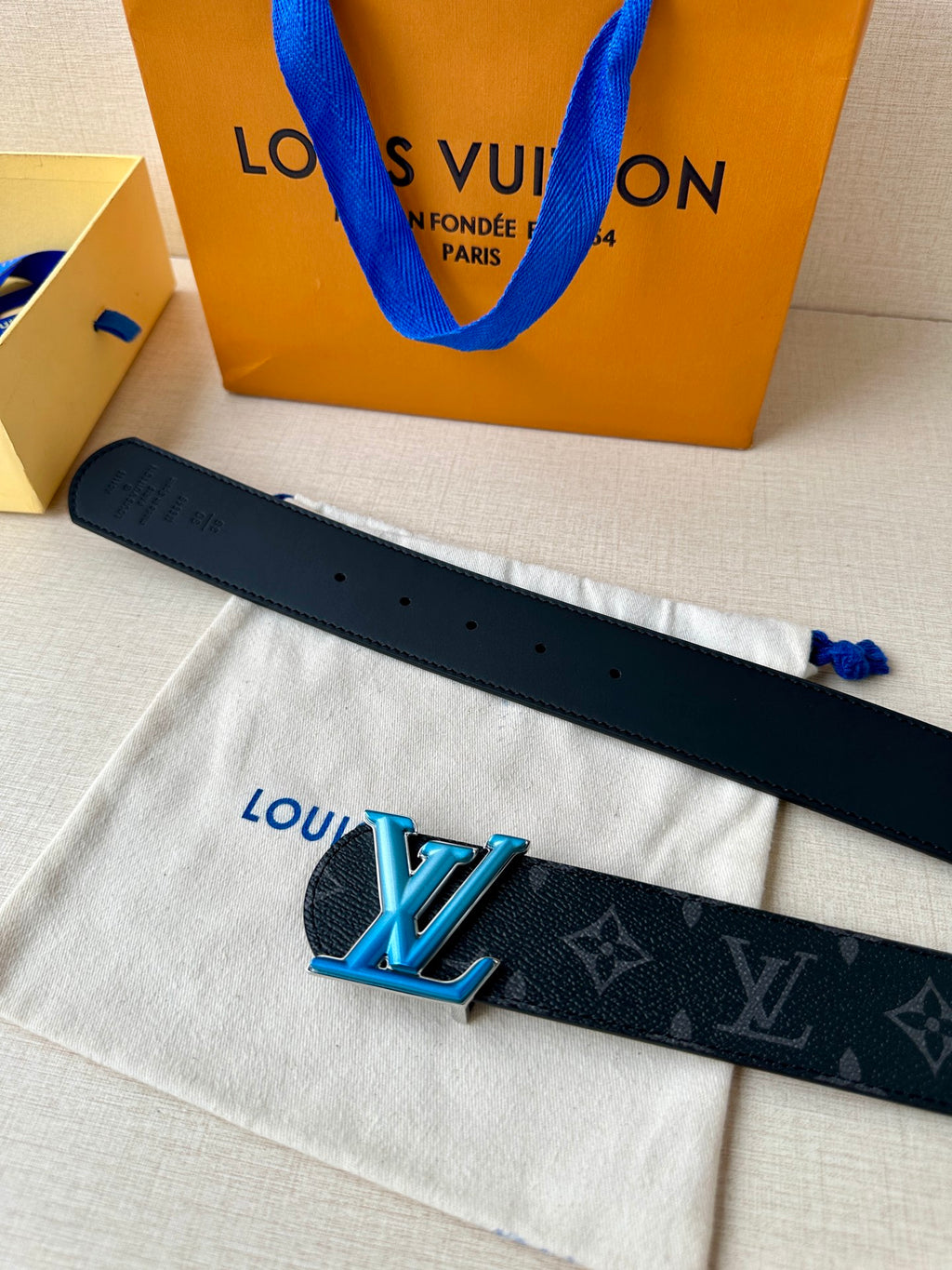 Louis Vuitton belt with dark strap, punched holes, and blue LV buckle front