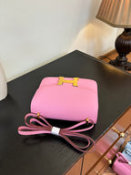 Pink leather handbag with top clasp and bow-tie strap, placed on dark tabletop