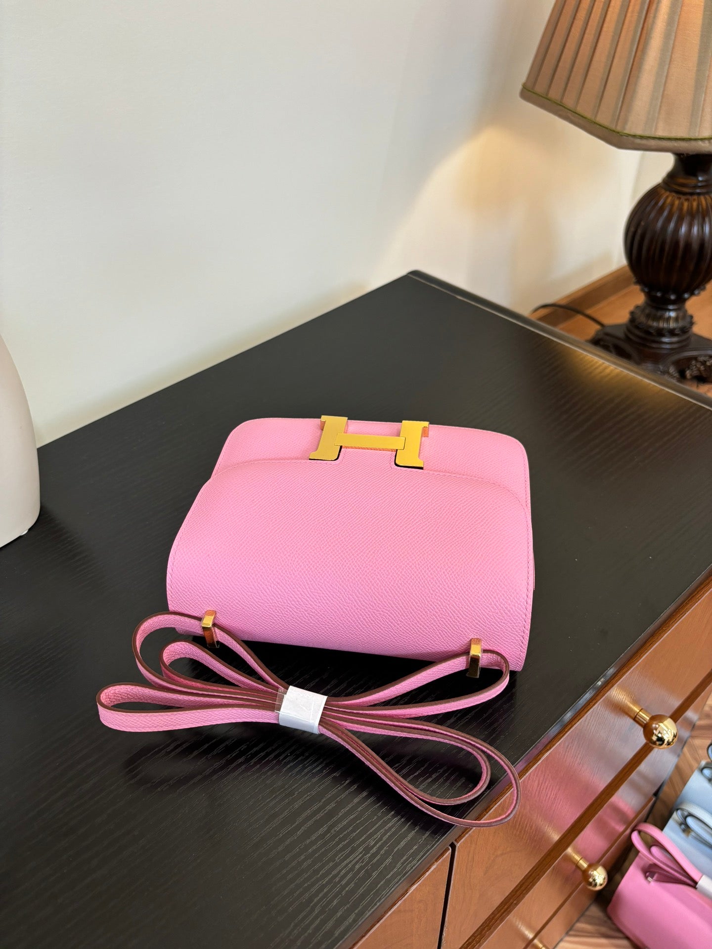 Pink leather handbag with top clasp and bow-tie strap, placed on dark tabletop