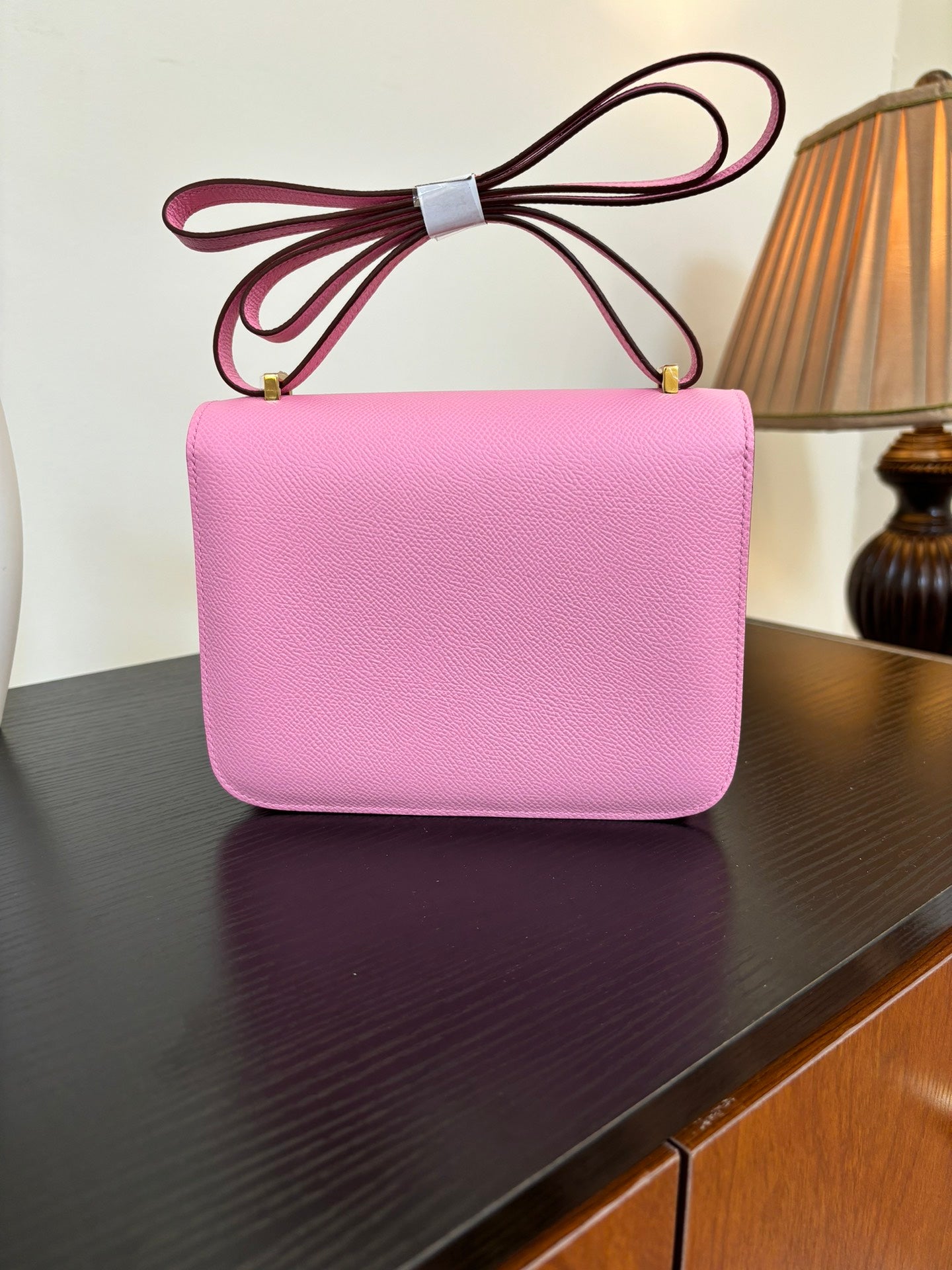 Pink leather handbag with flap front and gold H clasp, front view with tied handle