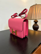 Hermes pink mini bag with gold H hardware and red crossbody strap, side view.