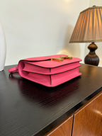 Hermes pink mini bag with flap and gold clasp, red crossbody strap, angled view.