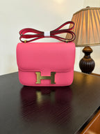 Hermes pink mini flap bag with gold H front clasp and red shoulder strap.