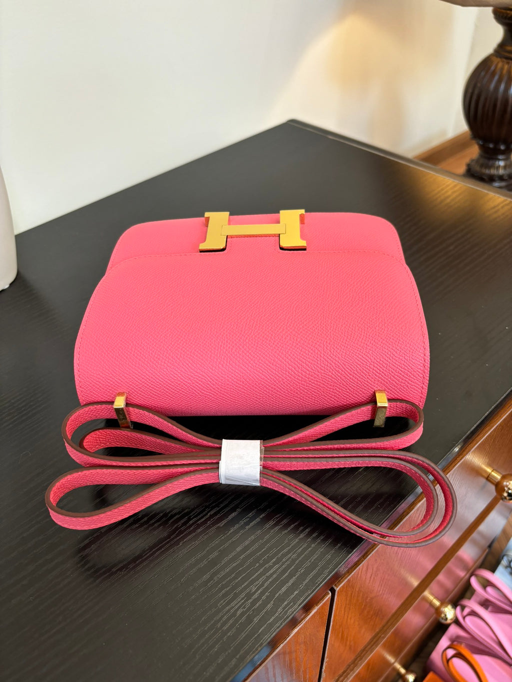 Hermes pink mini bag with gold H front clasp and red strap loop on tabletop.